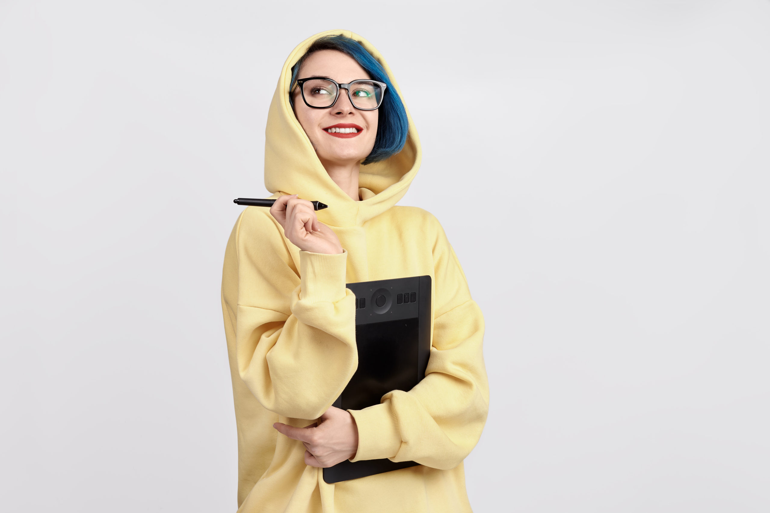 Young woman with blue hair and glasses in yellow hoodie holds a laptop or tablelet